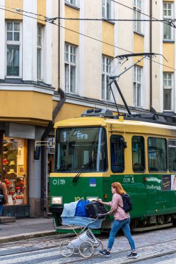 Helsinki, Finlandiya 22 Ağustos 2023. Genç bir kadın, Tasarım Bölgesi 'nde karşıdan karşıya geçmek için antika eşyalar taşıyan bir bebek arabası kullanıyor..