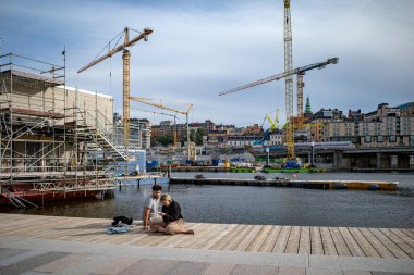 Stockholm, İsveç 29 Ağustos 2023. Genç bir çift büyük ölçekli inşaatın ortasında Slussen bölgesindeki rıhtımda oturuyor..