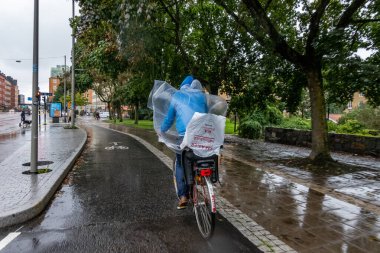 Stockholm, İsveç 1 Eylül 2023 Hornstull bölgesinde bir yağmur fırtınasında plastik yağmurluk giyen bir adam bisiklete biniyor.