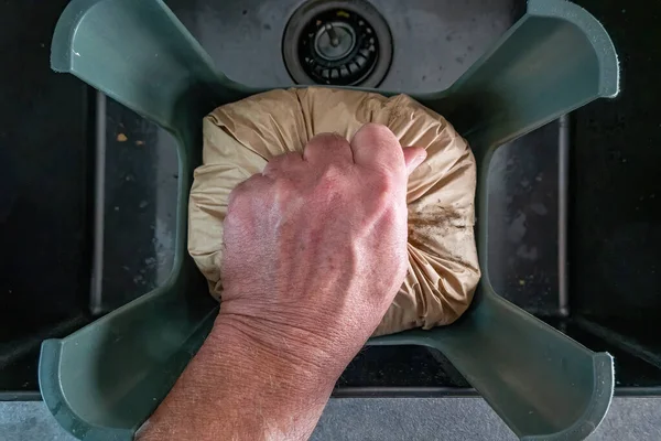 Stockholm, Sweden A hand grabs a brown bag of organic kitchen waste in a kitchen sink to take to recycling.