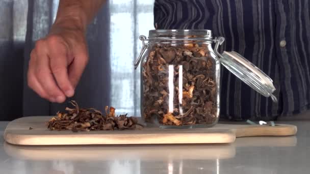瑞典斯德哥尔摩一个男人把野外采摘的 觅食的 晒干的长春花蘑菇放进桌子上的一个罐子里 — 图库视频影像