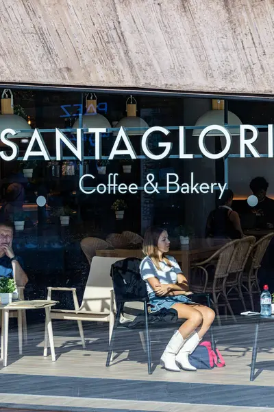 Porto, Portekiz 20 Eylül 2023. Kovboy çizmeli genç bir kadın Santa Gloria fırınının ve kafenin vitrininde oturuyor..