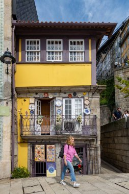 Porto, Portekiz 20 Eylül 2023 Bir turist Ribeira bölgesindeki küçük şirin sarı hediyelik eşya dükkanının önünden geçiyor.