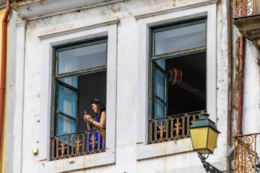 Porto, Portekiz 20 Eylül 2023 Ribeira bölgesindeki eski bir apartmanın penceresindeki bir kadın fotoğrafını çekmek için telefonunu kullanıyor..