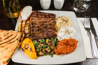 Tabouleh salatası, humus, ızgara biber ve ahşap masada pide ekmekli ızgara biftek..