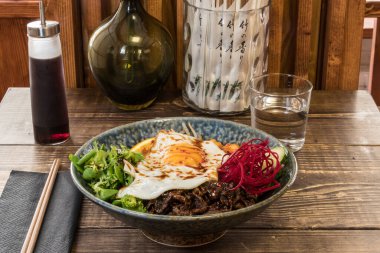 Bir tabak geleneksel Kore Bibimbap 'ı ve ahşap bir masada yumurta..