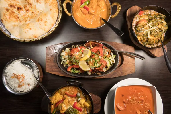 A presentation of different Indian dishes with Chicken Tikka Sizzlar in the middle  with rice and nan bread.