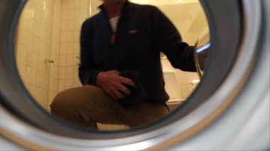 Bir adam çamaşır makinesini çamaşır makinesiyle dolduruyor.. 