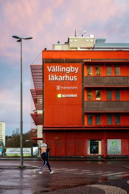 Stockholm, İsveç 24 Kasım 2023 Vallingby banliyösündeki bir meydanda İsveççe Valling Lakarhus ya da Vallingby Kliniği yazan bir tabelanın altında bir adam yürüyor..