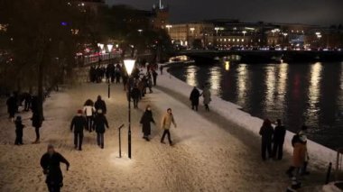 Stockholm, İsveçli yayalar gece vakti şehir merkezindeki rıhtımda karların üzerinde yürüyorlar.. 