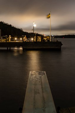 Stockholm, İsveç Ekero banliyösünde geceleri Malaren Gölü 'nde küçük bir rıhtım rüzgarda dalgalanan bir İsveç bayrağı..