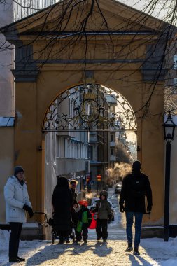 Stockholm, İsveç, 24 Aralık 2023 güneşli bir günde Katrain Kilisesi mezarlığında yürüyen yayalar ve Sodermannagatan 'a giden kemerli bir yol..