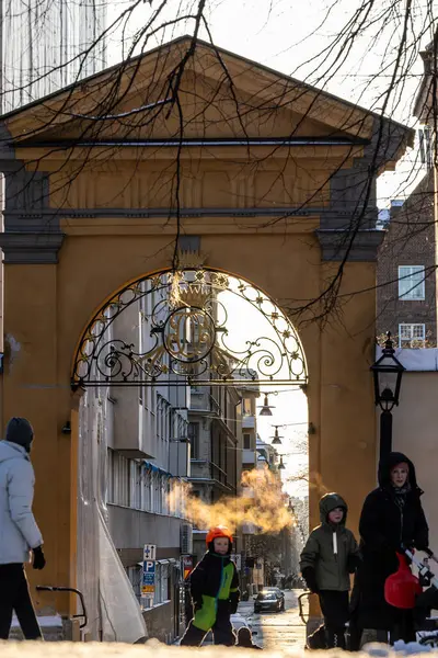 Stockholm, İsveç, 24 Aralık 2023 güneşli bir günde Katrain Kilisesi mezarlığında yürüyen yayalar ve Sodermannagatan 'a giden kemerli bir yol..