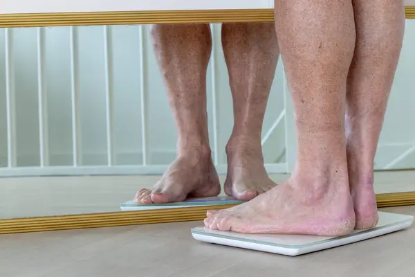 A man with dry winter feet weighs himself on a bathroom scale.