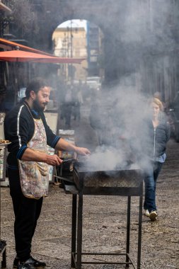 Palermo, Sicilya, İtalya 12 Ocak 2024 Bir aşçı Mercato di Ballaro sokak yiyecek pazarında sigara içilen bir ızgaranın yanında duruyor