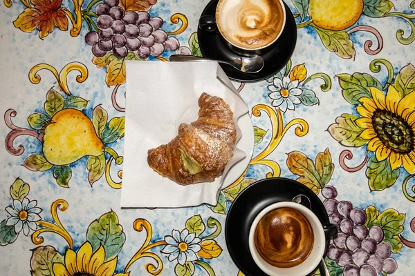 Cefalu, Sicily, Italy An italian breakfast with a pistachio croissant and coffees on a colorful table.