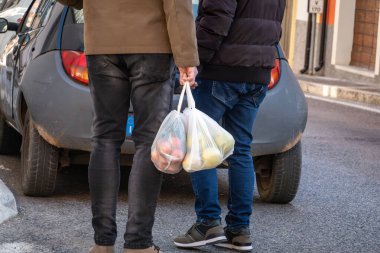Raiano, İtalya. 18 Şubat 2024. İki adam ellerinde bir torba meyveyle sokakta dikiliyorlar..