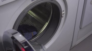 Bir adam çamaşır makinesini kıyafetlerle dolduruyor.