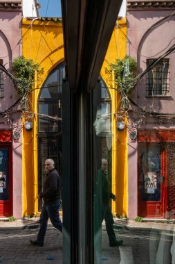 İstanbul, Türkiye 18 Mart 2024. Bir adam Balat bölgesinde renkli bir sokakta yürüyor ve bir giyim mağazasının camına yansıyor..