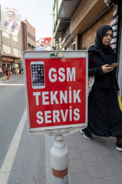 İstanbul, Türkiye 18 Mart 2024, Balat ilçesindeki GSM Teknik Servis veya telefon tamiratı yazan tabelanın önünden geçen yerli bir kadın,.