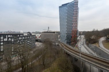Stockholm, İsveç Hammarbyhamnen bölgesindeki STHLM 01 binasından yüksek bir metro treni geçiyor..