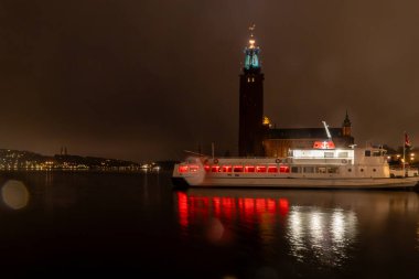 Stockholm, İsveç 29 Mart 2024 Stockholm Belediye Binası yağmurlu ve toplu taşıma feribotu geceleri pencerelerde kırmızı ışıkla kenetlendi..
