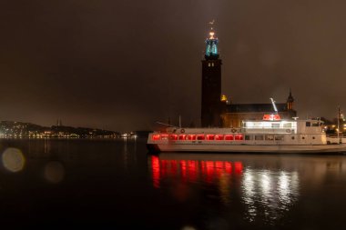 Stockholm, İsveç 29 Mart 2024 Stockholm Belediye Binası yağmurlu ve toplu taşıma feribotu geceleri pencerelerde kırmızı ışıkla kenetlendi..