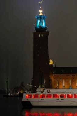Stockholm, İsveç 29 Mart 2024 Stockholm Belediye Binası yağmurlu ve toplu taşıma feribotu geceleri pencerelerde kırmızı ışıkla kenetlendi..