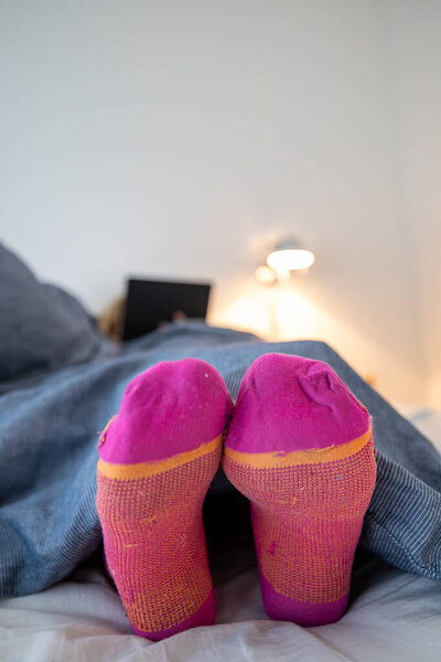 A woman's feet with socks underneath big down comforter in a bedroom.