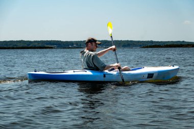 Broomes Island, Maryland USA A young man kayaks on the Patuxent River on a sunny day. clipart