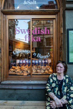 Stockholm, İsveç 17 Mayıs 2024 Bir kadın fırın penceresinin altında İsveç fika ve tarçınlı çöreklerle oturuyor.