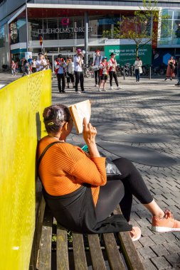 Stockholm, İsveç 21 Mayıs 2024 'te bir kadın, AB parlamento seçimlerini destekleyen bir etkinlikte Liljeholmen meydanındaki sokak müzisyenlerini dinlerken kendini güneşten koruyan bir bankta oturuyor..