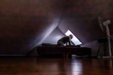 Danimarka 'nın Tisvilde şehrinde bir adam tavan arası yatak odasının içinde bir yatak ve mansard çatısı olan bir yatakta oturuyor..