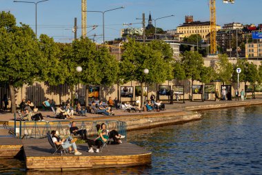 Stockholm, İsveç 17 Haziran 2024 İnsanlar Riddarfjarden 'da yaz akşamı güneşinde Gama Stan veya Old Town' da sanatsal bir kumsalda oturuyorlar..