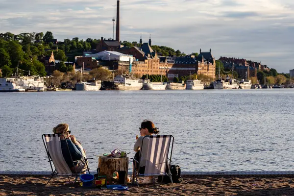 stock image Stockholm, Sweden June 17, 2024 People sitting on an artifical sandy beach at Gama Stan or Old Town in the summer evening sun on Riddarfjarden.