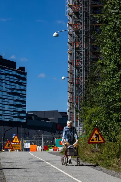 stock image Stockholm, Sweden June 20, 2024 A senior man walks on a bike path with a walker past the landmark Mall of Scandinavia buildings in the Solna suburb and train tracks.