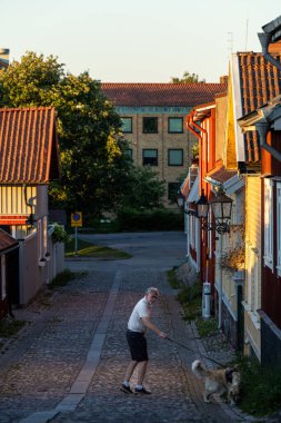 Gavle, İsveç 25 Haziran 2024 Kıdemli bir adam köpeğini Gamla Gefle tarihi bölgesindeki eski evlerin arasında gezdiriyor..