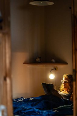 Yatakta uzanmış kitap okuyan bir kadın.