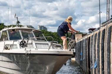 Stockholm, Sweden July 26, 2024 A woman on a motorboat uses a line to tie up to the walls of the Hammarby Lock to enter the Baltic Sea from Lake malaren. clipart