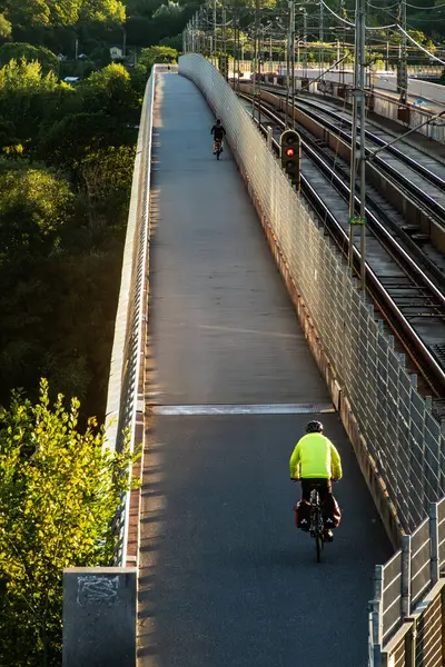 stock image Stockholm, Sweden Aug 13, 2024 A bicyclist in the early morning crosses the Arsta train bridge on a bike path.