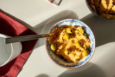 Bir kasede zeytin ve kaşık servis eden humus..