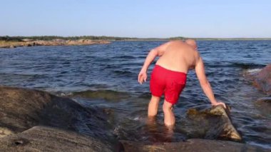 İsveç, Oregrund 'da kırmızı şortlu bir adam kaygan kayalıklardan yüzmek için soğuk Baltık Denizi' ne girer.. 