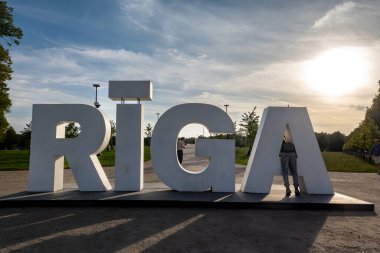 Riga, Latvia Sept 9, 2024 Pedestrians and a  large Riga sign in white letters in a public park. clipart