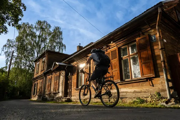 stock image Riga, Latvia Sept 9, 2024 A bicyclist in the Zemgale Suburb  on the left bank of the Daugava River past old wooden houses.