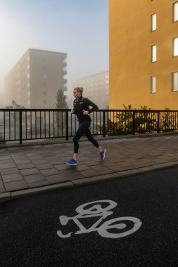 Stockholm, Sweden Sept 19, 2024 A jogger on the sidewalk next to  a bike path in the Hornstull district on a foggy morning. clipart