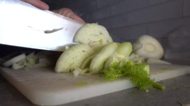 Bir aşçı, evcil bir mutfakta kesme tahtasına rezene dilimliyor..