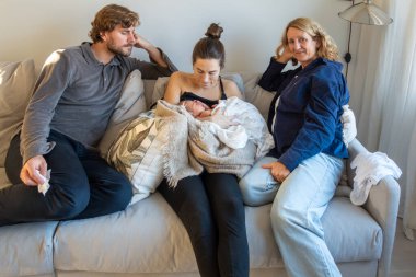 Stockholm, İsveç. Yeni doğmuş bir bebeği olan genç bir anne ve baba anne ve büyükannesiyle birlikte kanepede oturuyor.. 