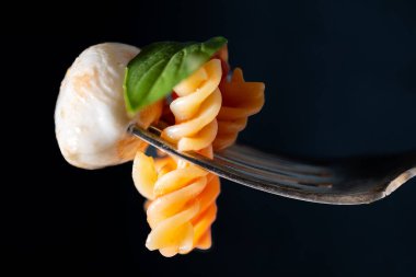Domates soslu fusilli makarna ve mozzarella topu ve fesleğen yaprağı içeren gümüş çatalın yakın çekimi..