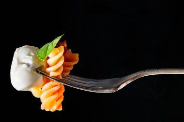 Domates soslu fusilli makarna ve mozzarella topu ve fesleğen yaprağı içeren gümüş çatalın yakın çekimi..