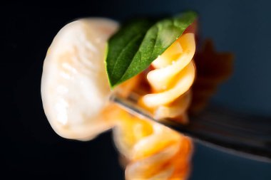 Domates soslu fusilli makarna ve mozzarella topu ve fesleğen yaprağı içeren gümüş çatalın yakın çekimi..
